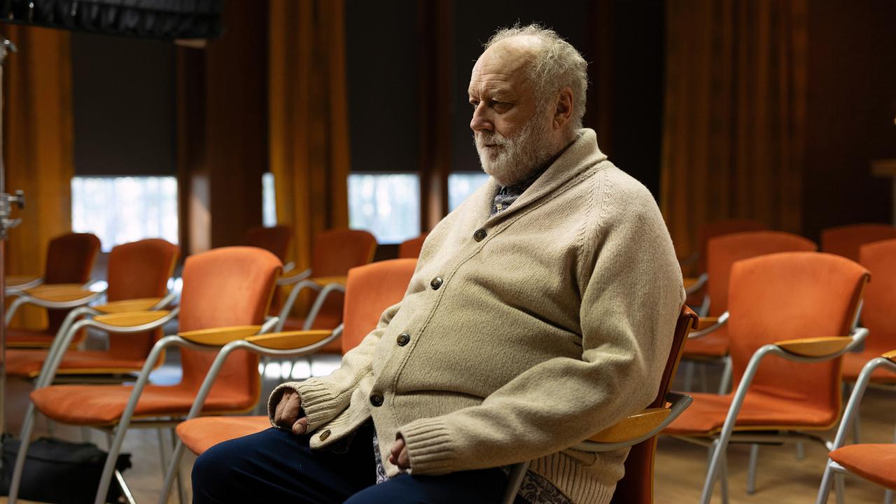 Musikpädagoge Gustav König sitzt allein in einem Saal mit leeren Stuhlreihen.