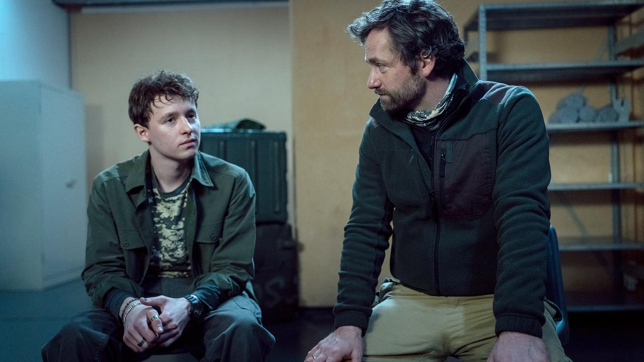 Nahaufnahme von Moritz Zechmann und Sohn Mats, die nebeneinander im Bunker beim Survivalkurs sitzen.