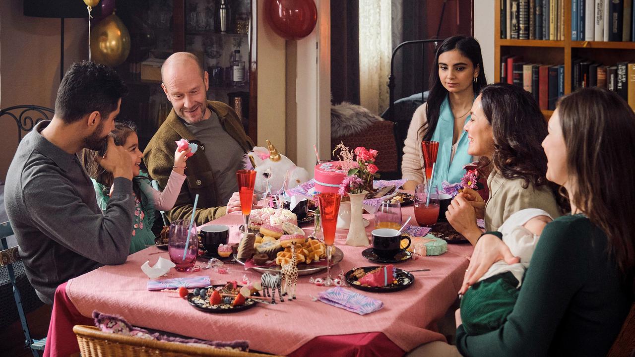 Bei der bunt dekorierten Geburtstagsfeier  ihrer Nichte sitzt Nelly mit ihrer Familie um einen Tisch mit Kuchen und Luftballons.