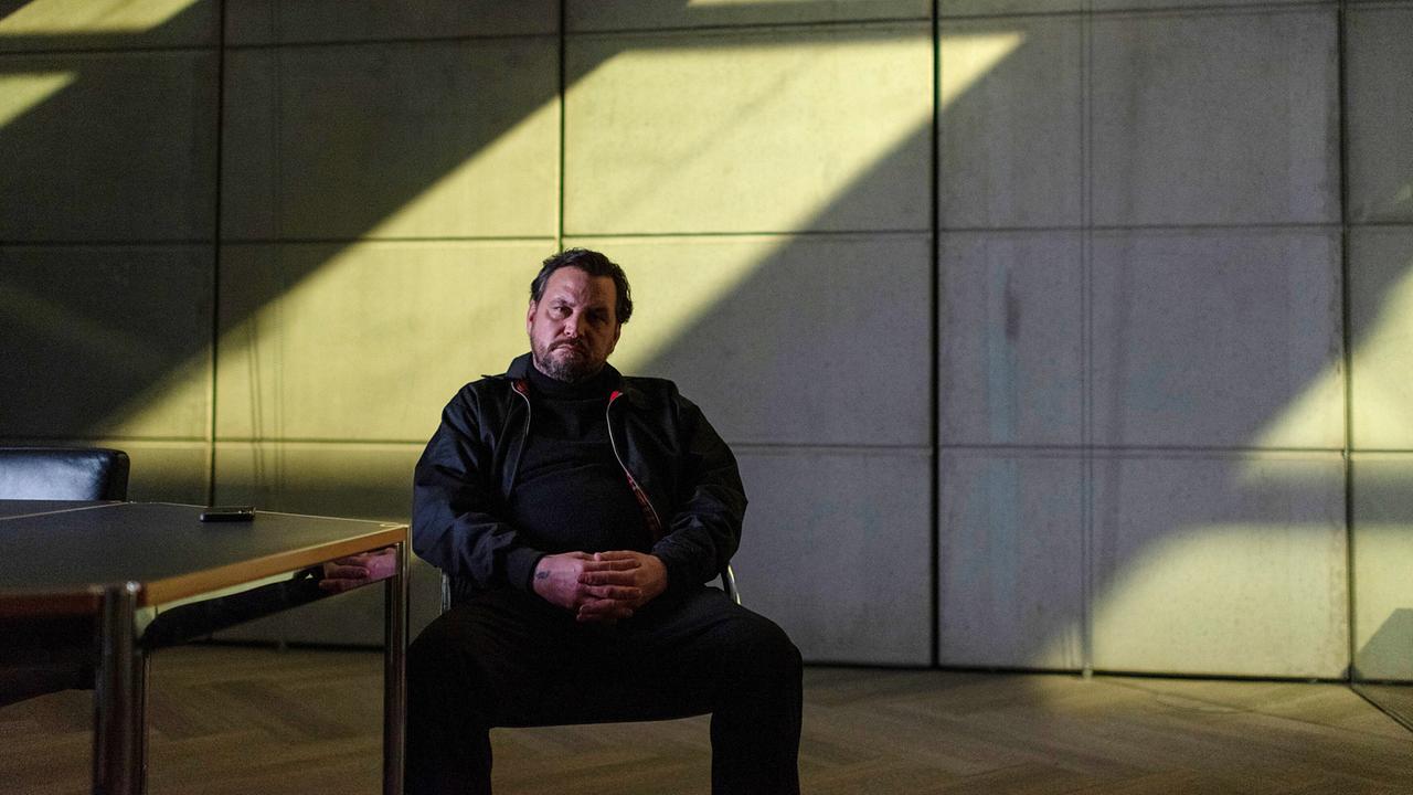 Franco Steiner, Mitarbeiter der Firma Prometheus, hat „aufgeräumt“ und sitzt in einem kargen Raum vor einem Tisch.