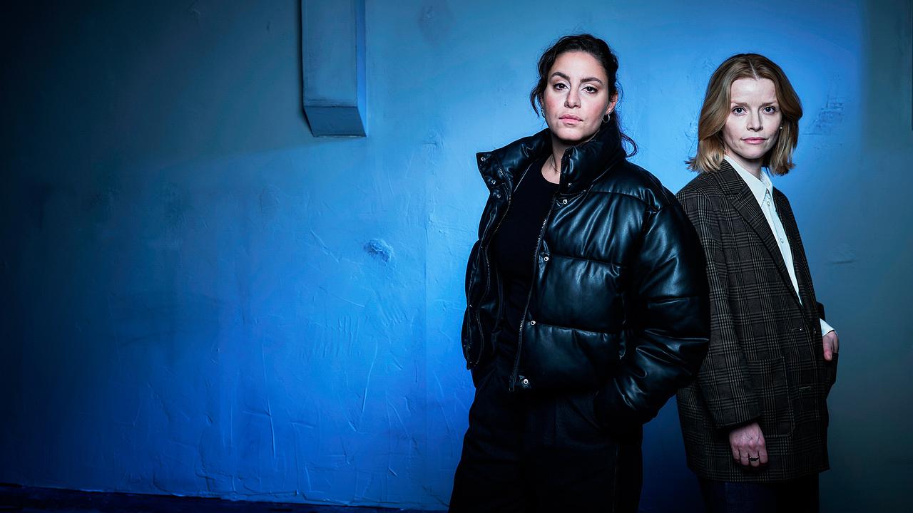 Mila Sahin und Elli Krieger stehen vor einer blau beleuchteten Wand.