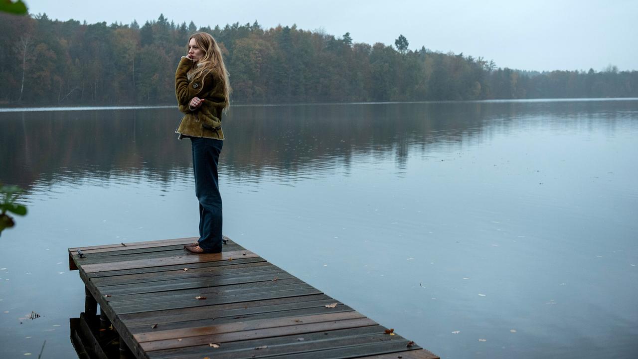 Anna Nowak steht allein auf einem Steg an einem stillen, nebligen See.