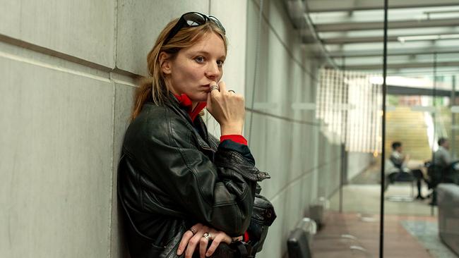 Anna Nowak in Lederjacke lehnt nachdenklich an einer Betonwand in einem modernen Büroflur.