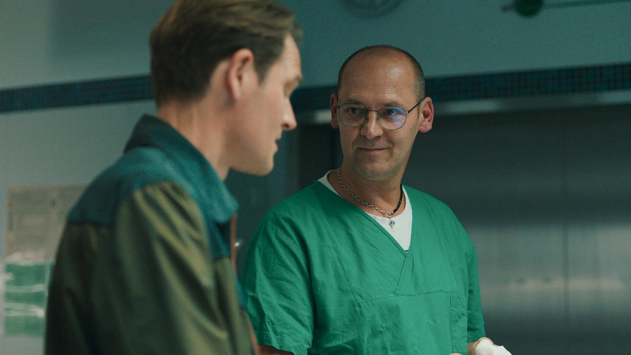 Der Pathologe Petr in grüner OP-Kleidung erläutert Felix Voss die Todesursache des Opfers.