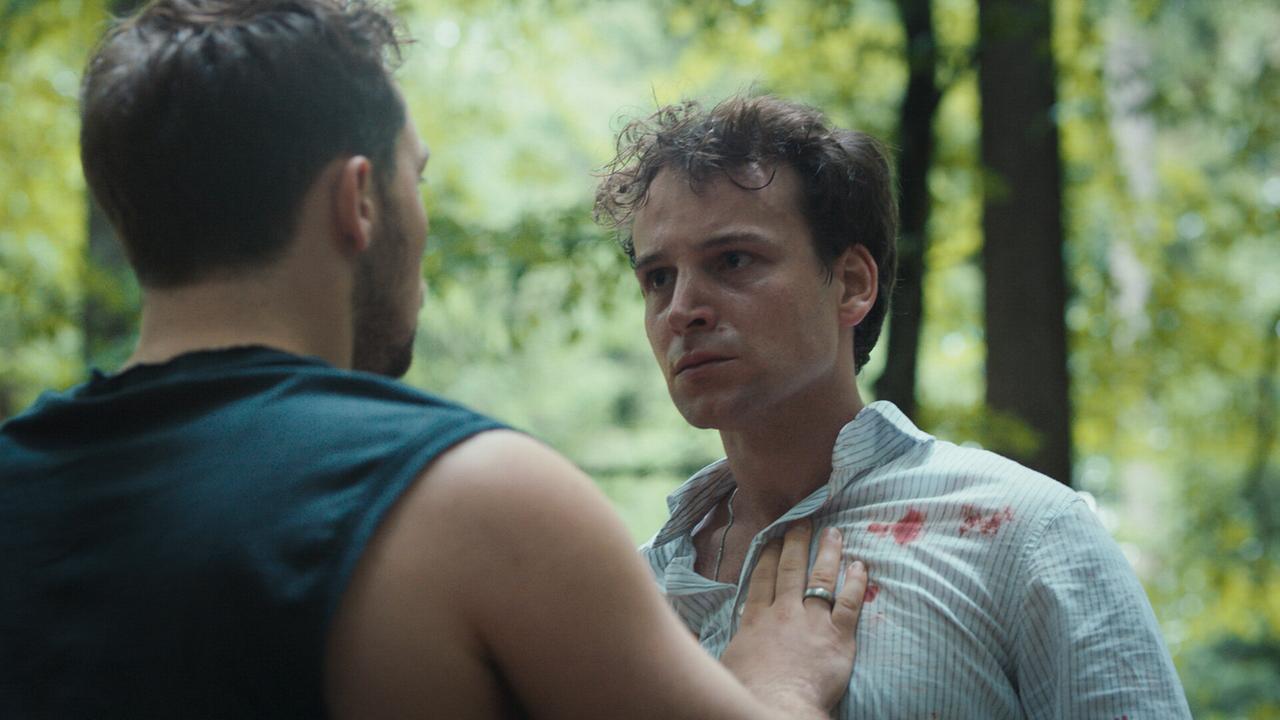 Marcel und Toni stehen sich im Wald angespannt gegenüber, einer davon mit blutverschmiertem Hemd. Marcel versucht seinen Freund Toni  zu beruhigen.
