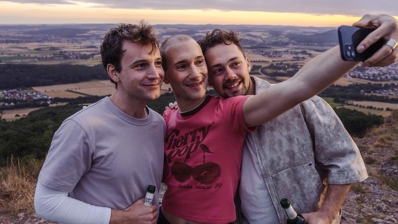 Die drei Freunde Toni Steeg, Elias Schaller und Marcel Dahlmann machen gemeinsam bei Sonnenuntergang auf dem Staffelberg ein Selfie  und halten Bierflaschen in den Händen.