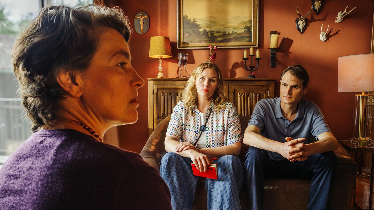Frau Schaller spricht in ihrem Wohnzimmer mit Kriminalhauptkommissarin Emmy Rathgeber und Kriminalhauptkommissar Felix Voss auf dem Sofa.
