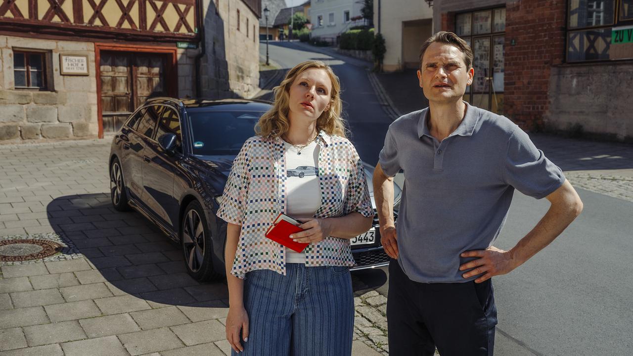 Kriminalhauptkommissarin Emmy Rathgeber und Kriminalhauptkommissar Felix Voss stehen bei Sonnenschein vor dem Haus Widner in Gottesgarten.