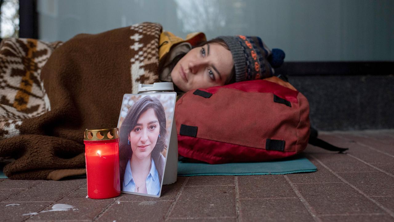 Wer hat Francesca getötet? Ihre Schwester Chiara harrt am Polizeipräsidium aus und liegt eingehüllt in Decken neben ihrem Rucksack auf dem Boden, vor ihr stehen eine brennende Kerze und ein Foto von Francesca.