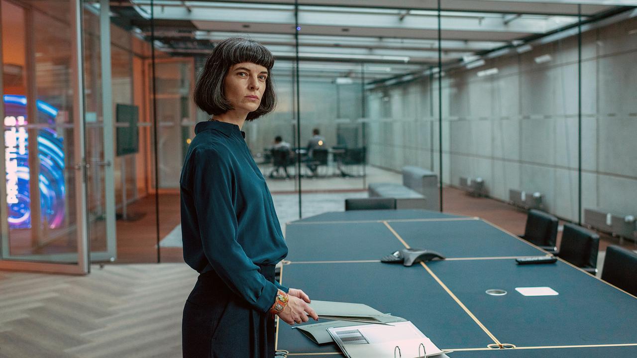 Viola Berger, die Geschäftsführerin von Prometheus, steht mit Akten an einem Konferenztisch in einem modernen, verglasten Büro.