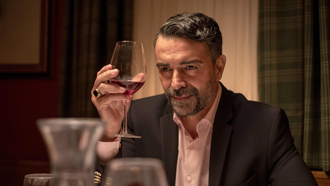 Luca Pelosi, ein elegant gekleideter Mann, hebt in einem Restaurant ein Glas Rotwein und blickt direkt in die Kamera.