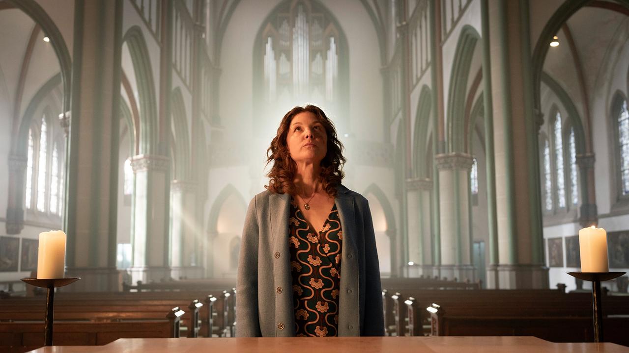 "Tatort: Man stirbt nur zweimal": Doreen Prätorius (Cordelia Wege) steht im sanften Licht der Münsteraner Kirche, das durch die hohen Fenster strömt. Mit einem Ausdruck von Ehrfurcht und Entschlossenheit blickt sie zum Altar und sucht in der sakralen Umgebung nach Antworten – oder Vergebung?