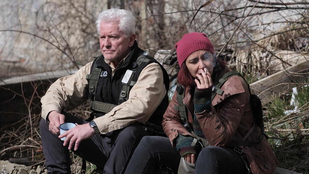 "Tatort: Charlie": Hauptkommissar Ivo Batic (Miroslav Nemec) sitzt mit Mila Kovac (Dorka Gryllus) auf dem Hauptplatz in Übungsheim und unterhalten sich über die Military Police, die gerade eintrifft.