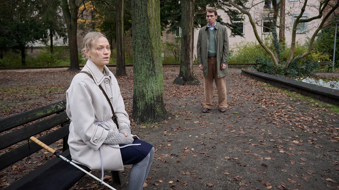 "Tatort: Ich sehe dich": Lisa Blum (Mavie Hörbiger) sitzt auf einer Bank im Park und wird von Stephan Gellert (Alexander Simon) beobachtet.