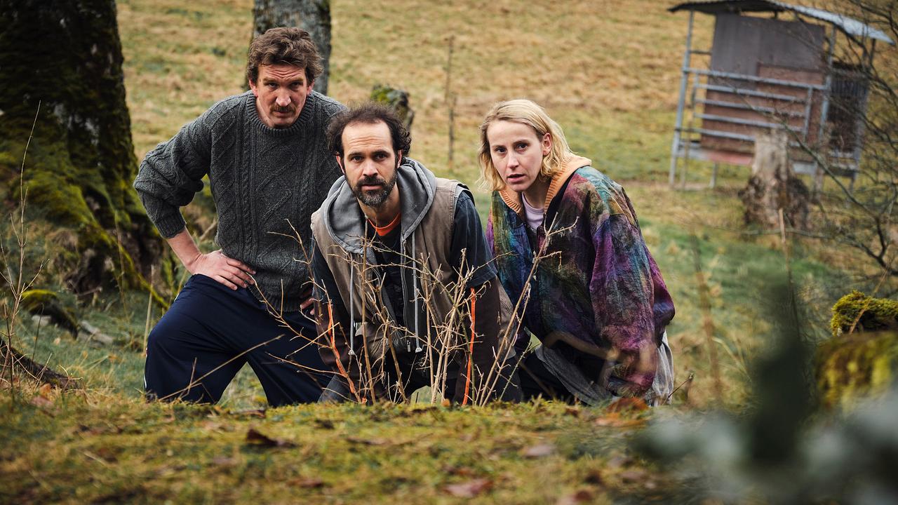 Felician Hohnloser, Karsten Antonio Mielke und Mareike Beykirch hocken im Gras und betrachten etwas an einem Waldrand.
