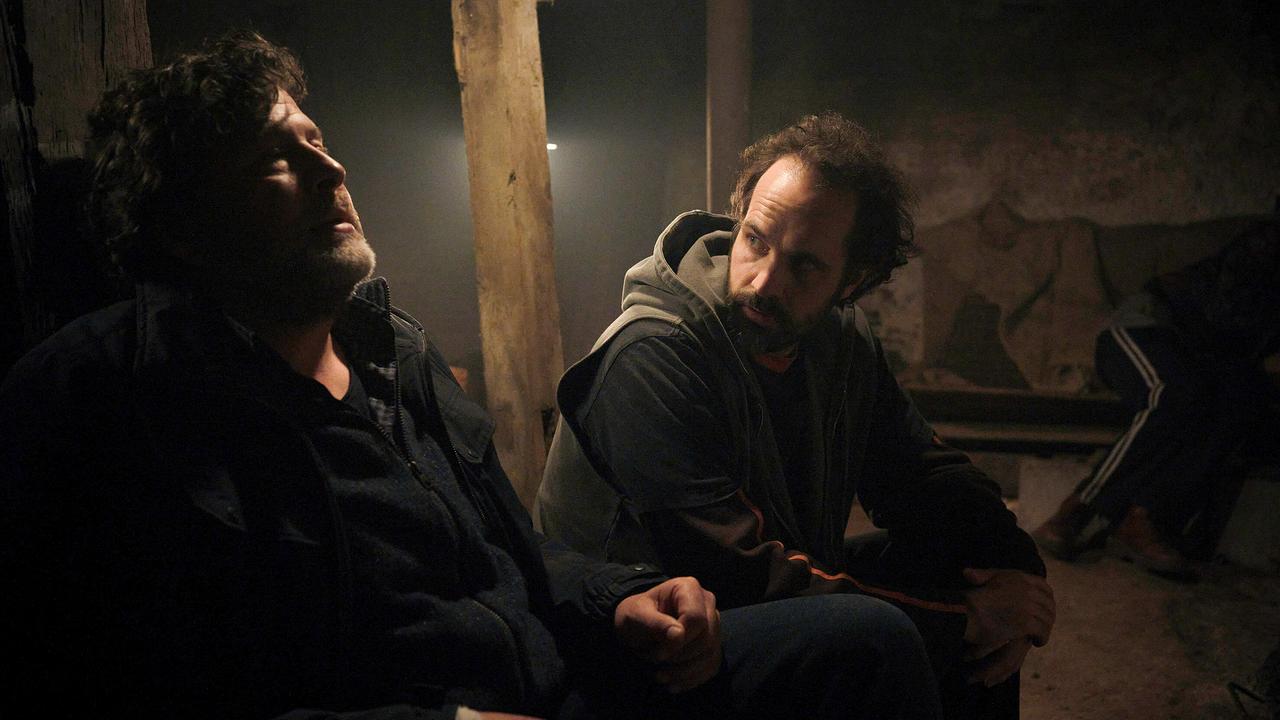 Hans-Jochen Wagner und Felician Hohnloser sitzen nebeneinander in einem dunklen Keller.