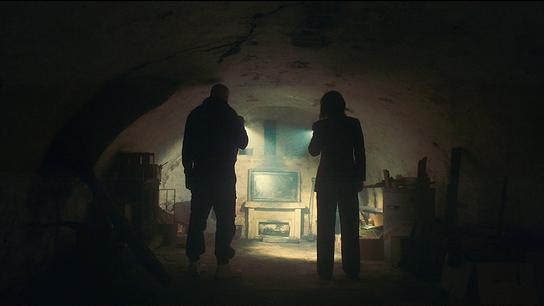 Edin Hasanovic und  Melika Foroutan mit Taschenlampen erkunden einen niedrigen, dunklen  Raum eines Kellergewölbe.