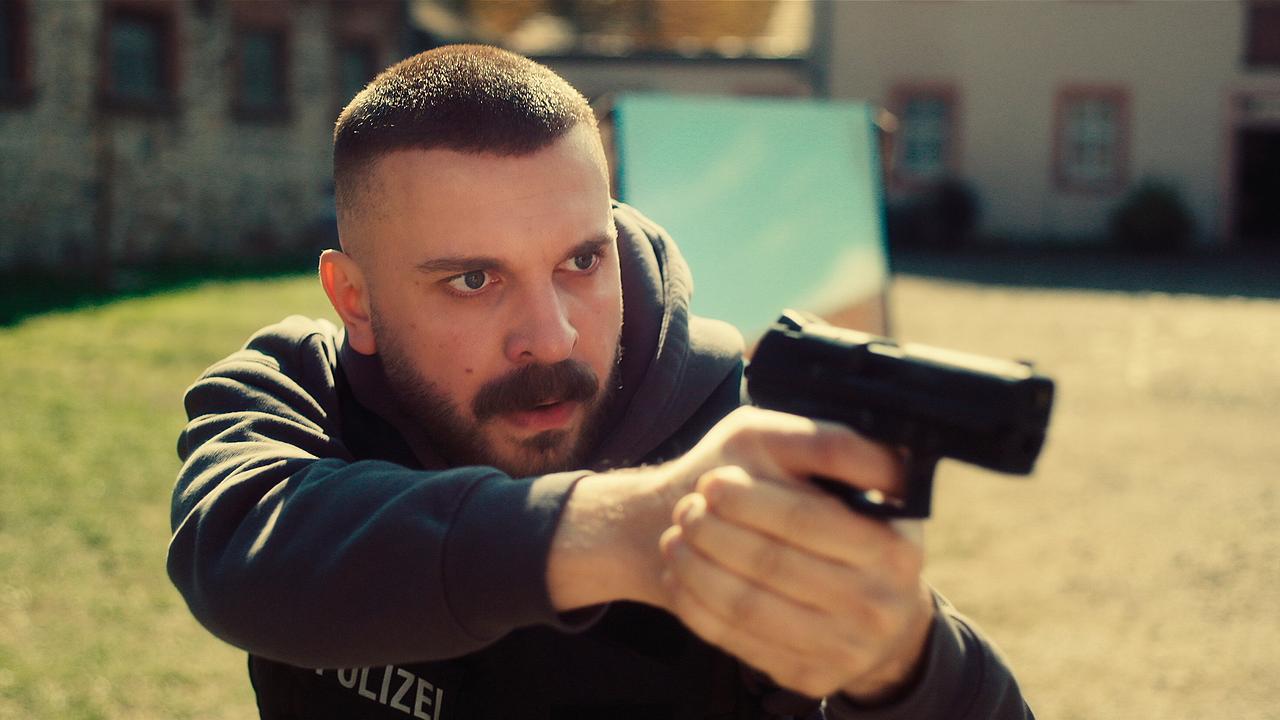 © ORF/HR/Sommerhaus Edin Hasanovic zielt mit einer Pistole in einem Hof zwischen alten Gebäuden.