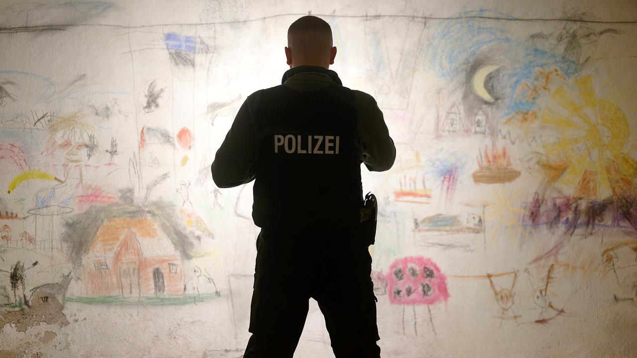 © ORF/HR/Sommerhaus/Daniel Dornhöfer Edin Hasanovic in Polizeiweste betrachtet eine Wand voller bunter Kinderzeichnungen.