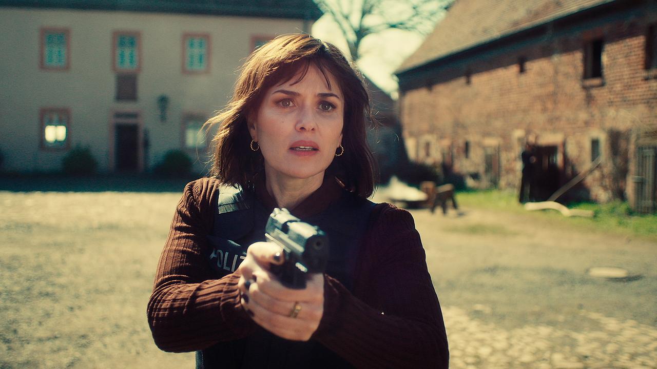 © ORF/HR/Sommerhaus Melika Foroutan zielt mit einer Pistole in einem Hof zwischen alten Gebäuden.