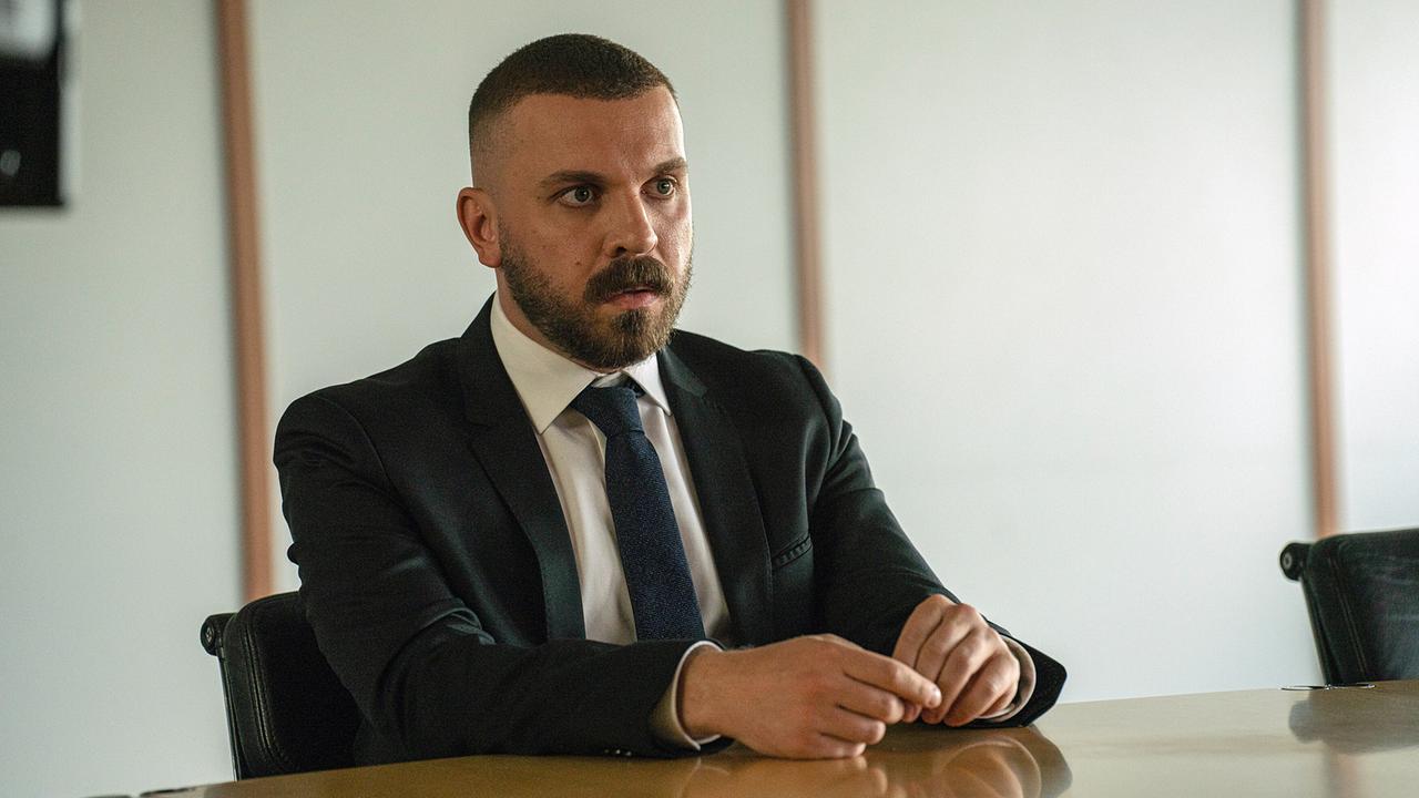 © ORF/HR/Sommerhaus/Daniel Dornhöfer Edin Hasanovic im Anzug sitzt an einem Konferenztisch.