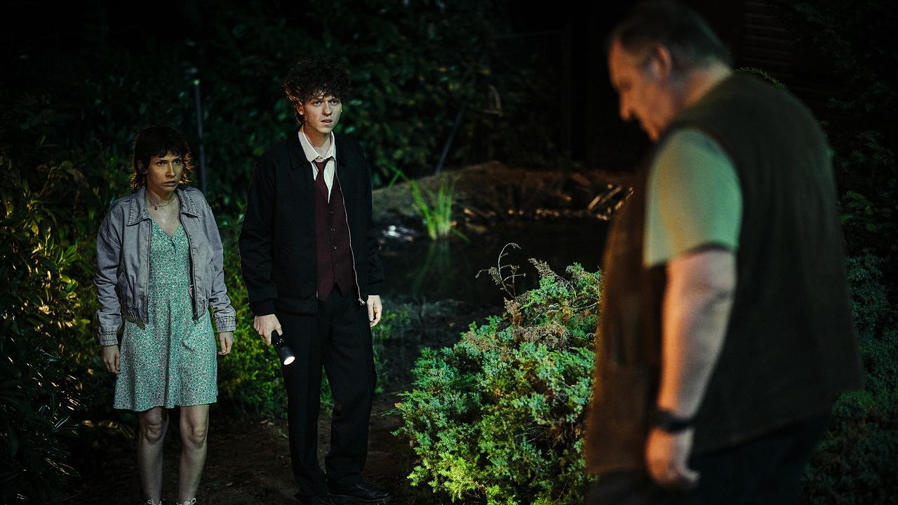 Nisha und Mike stehen nachts mit einer Taschenlampe am Ufer eines Teiches, während Nachbar Erwin Ramthor sich nähert.