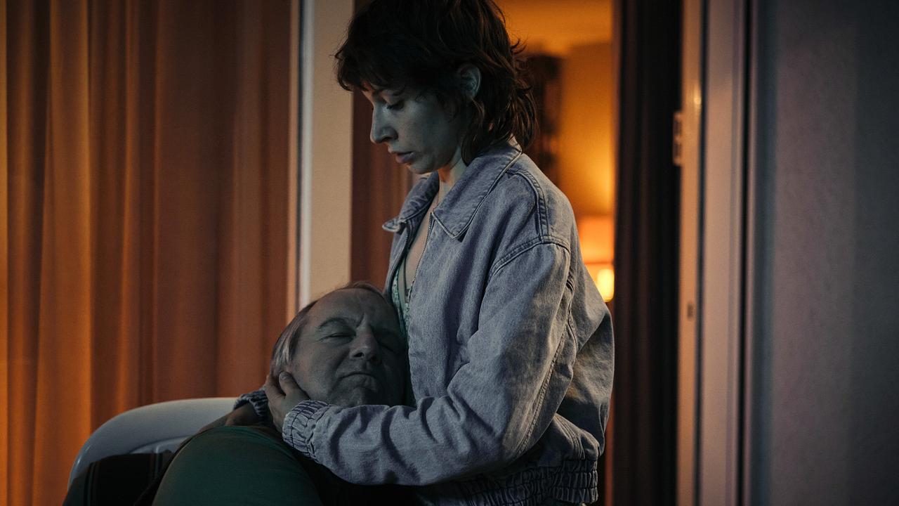 Nachbar Ramthor und Nisha umarmen sich in einem schwach beleuchteten Raum.