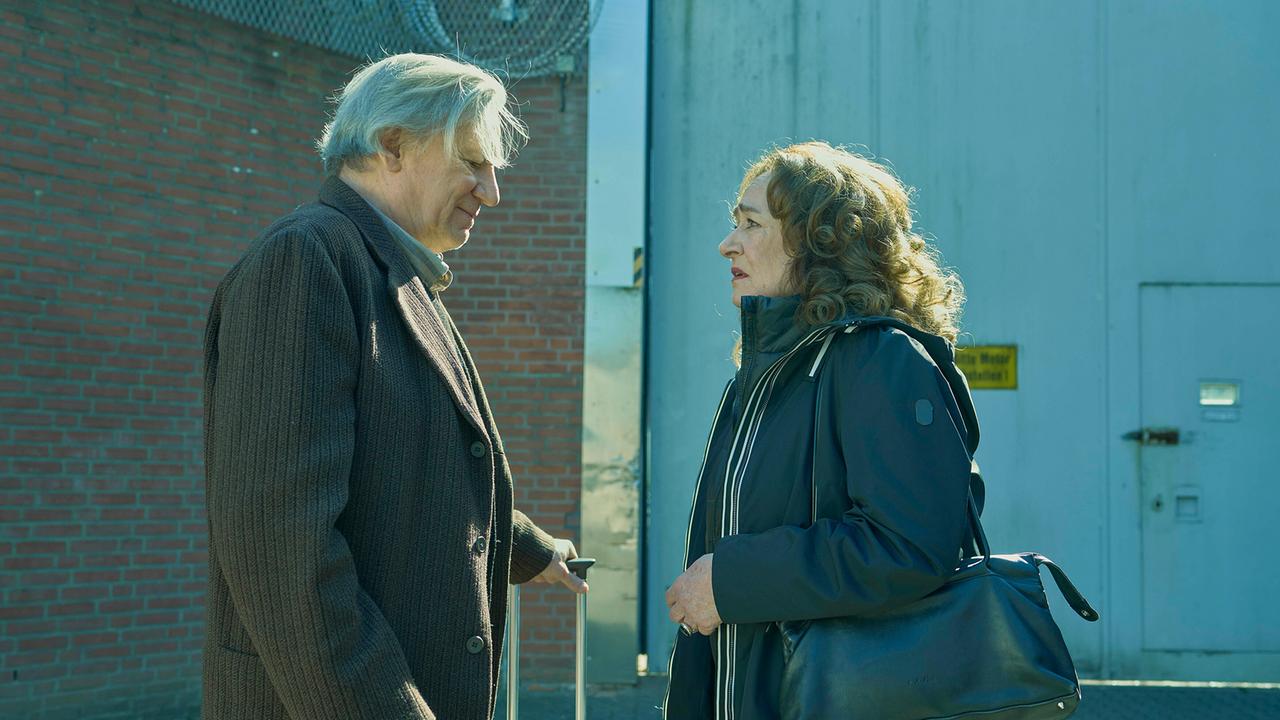 Kurt Hobrecht sen.  mit einem Rollkoffer unterhält sich mit Staatsanwältin Klemm draußen vor einem Gebäude.