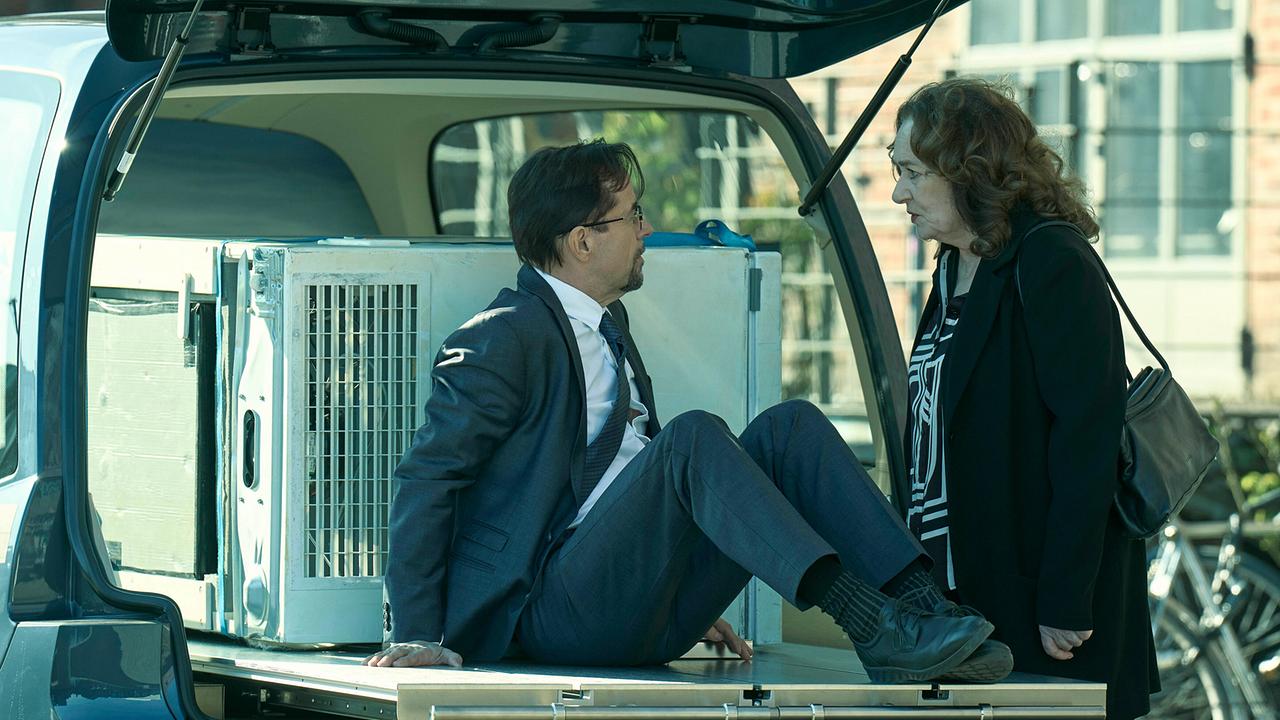 Prof. Karl Friedrich Boerne sitzt im offenen Kofferraum neben einer Kühltruhe mit einer tiefgefrorenen Leiche  und spricht mit Staatsanwältin Wilhelmine Klemm, die davor steht.