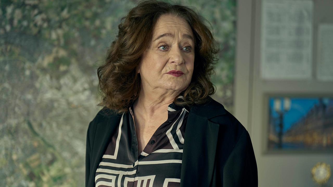 Staatsanwältin Wilhelmine Klemm in gemusterter Bluse steht vor einer großen Landkarte in ihrem Büro.