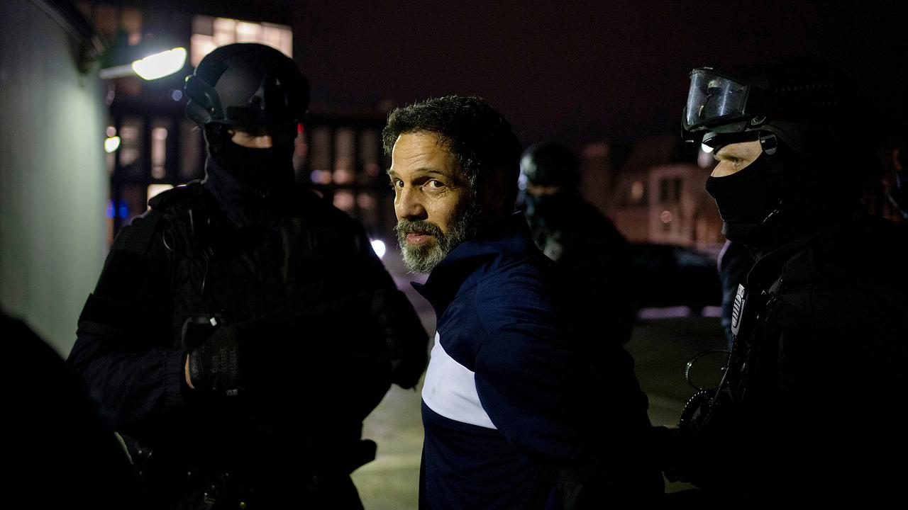 Zwei  Polizisten in Einsatzkleidung nehmen Mafiaboss Momodou bei Nacht fest.