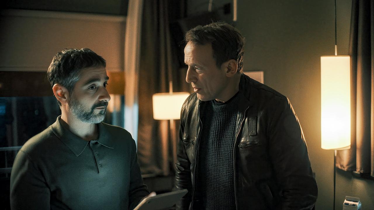 Falke und sein neue Kollege Mario Schmitt stehen abends in einem Raum und betrachten gemeinsam ein Tablet.