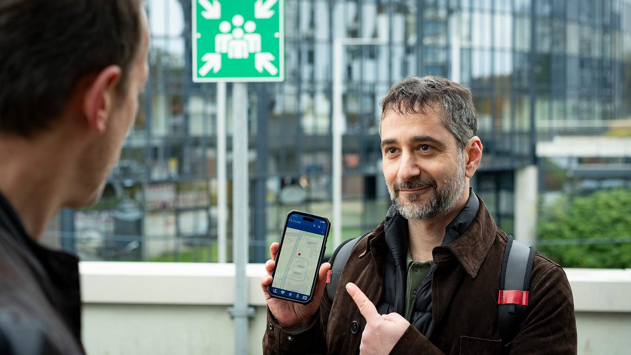 Neukollege Mario Schmitt zeigt Falke auf einem Smartphone eine Karte mit einem markierten Standort.