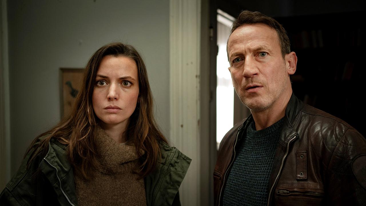 Lynn de Baer und Falke stehen nebeneinander in einem Innenraum und schauen nach vorne.