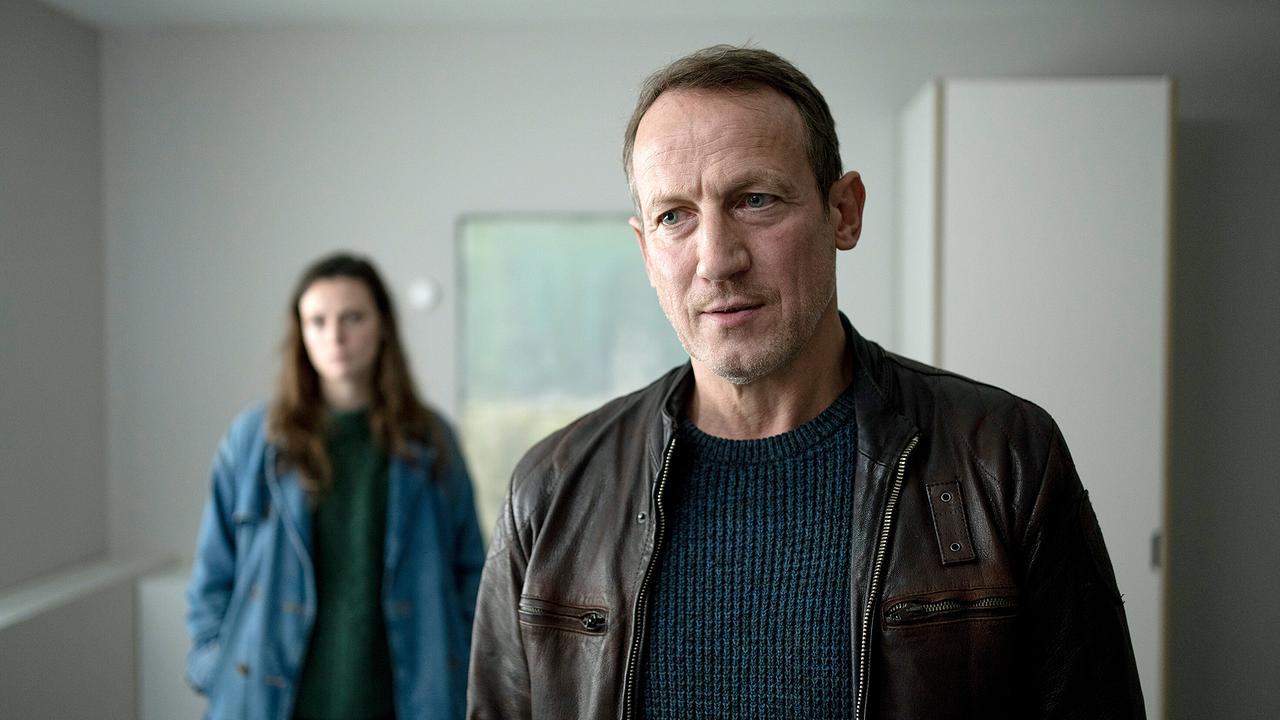 Lynn de Baer und Thorsten Falke befinden sich in einem schlichten Raum.