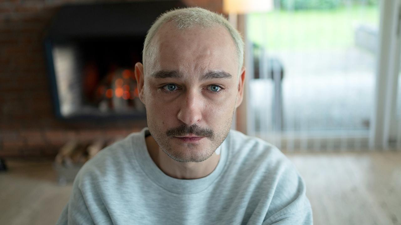 Carsten Kellmann mit blond gefärbten Haaren sitzt in einem Wohnzimmer mit Kamin im Hintergrund.