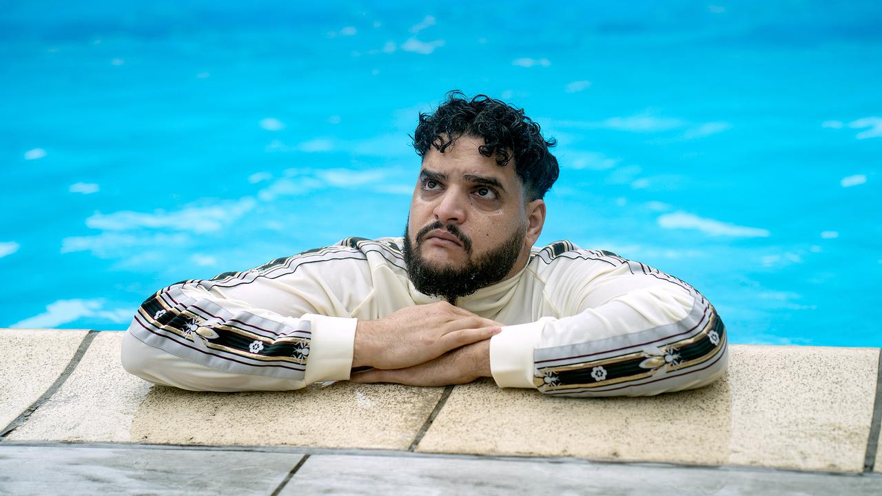 Karim Saidi, Sohn von Drogenboss Momodou, mit voller Bekleidung in einem Swimmimgpool, lehnt ernst blickend am Rand des Pools mit den Armen auf dem Beckenrand.