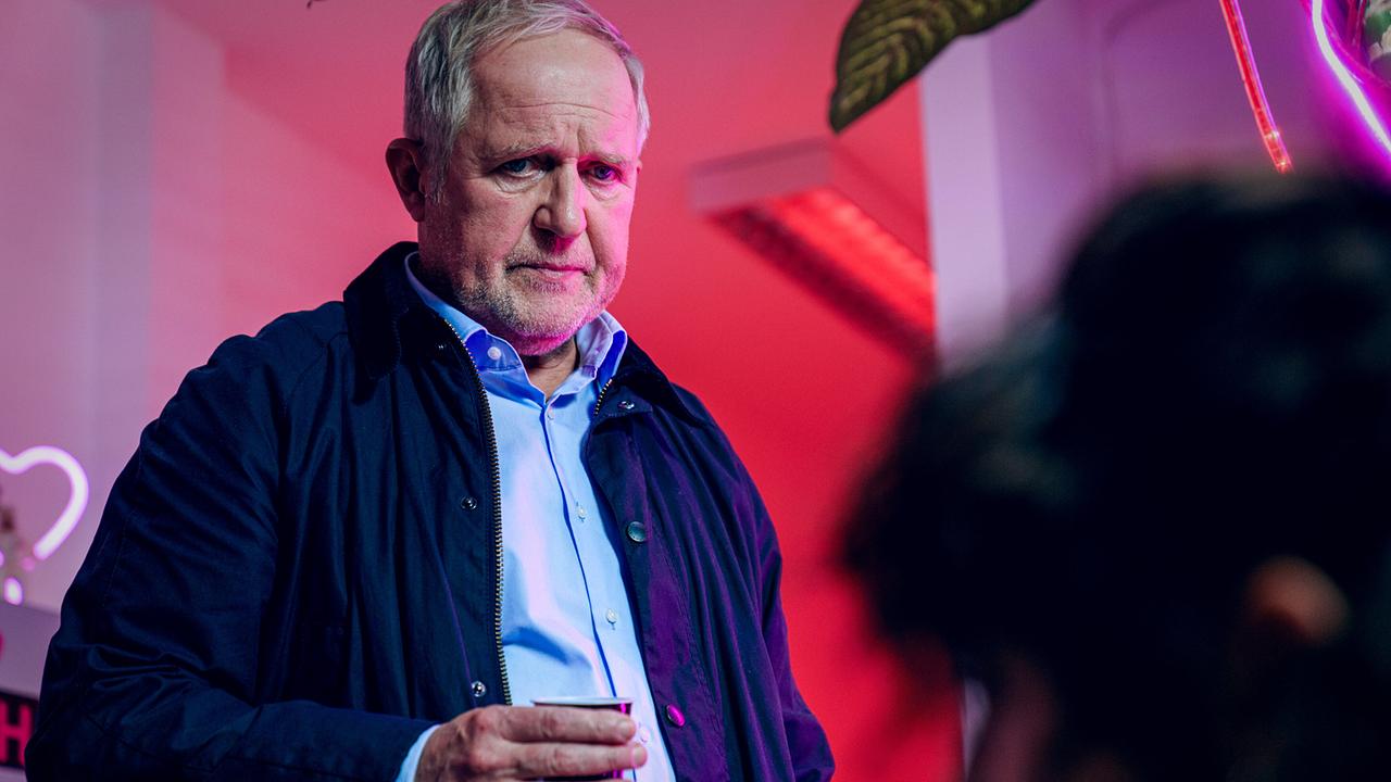 Moritz Eisner hält einen Kaffeebecher in einem Raum mit pinker Neonbeleuchtung.