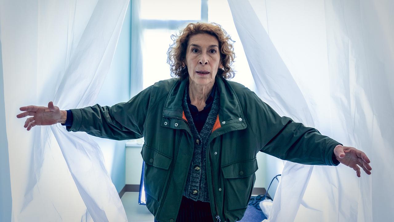 Bibi Fellner öffnet weiße Vorhänge und betritt einen hellen Raum.