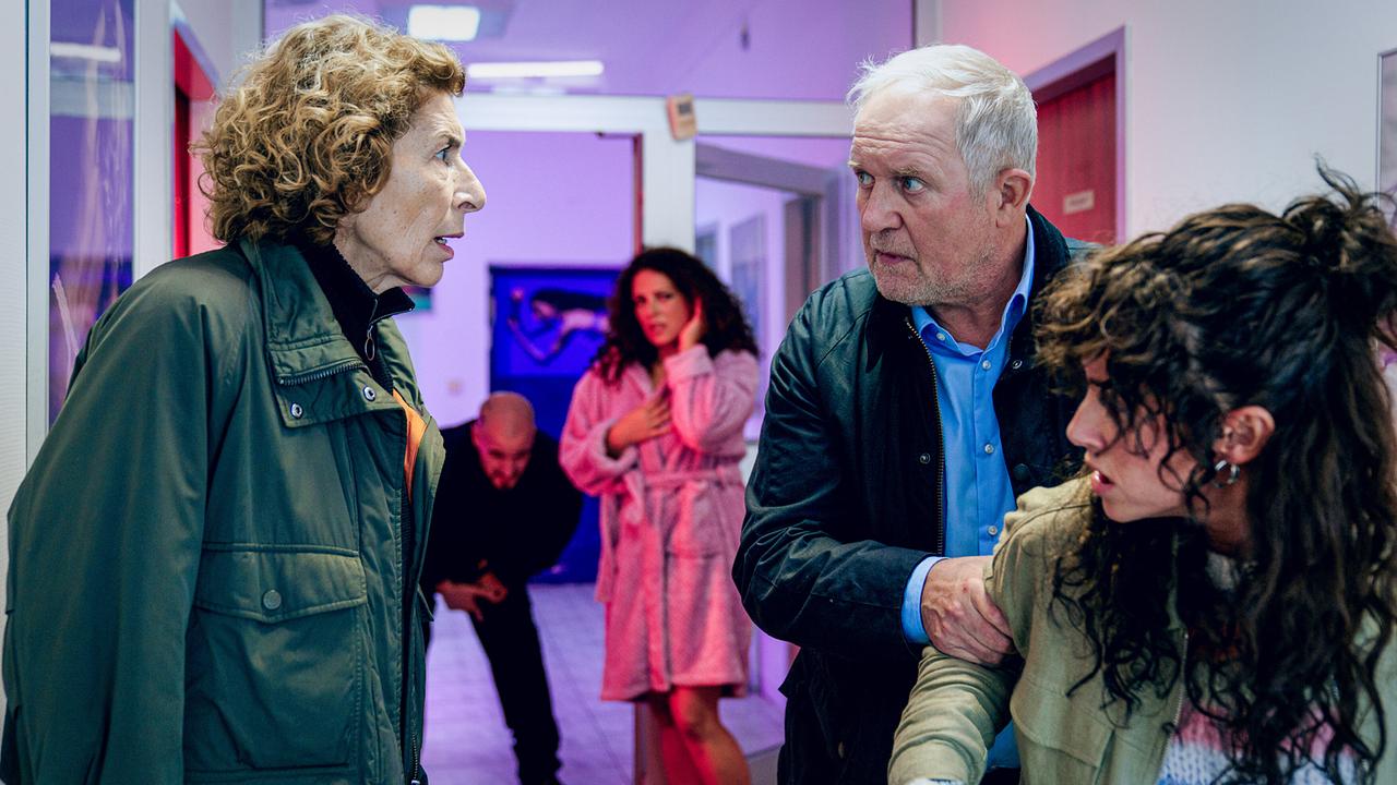 Bibi Fellner und Moritz Eisnerm der Linda Filipovic am Arm hält, blicken sich einem Gang an. Im Hintergrund stehen Romana und ein Mann. 