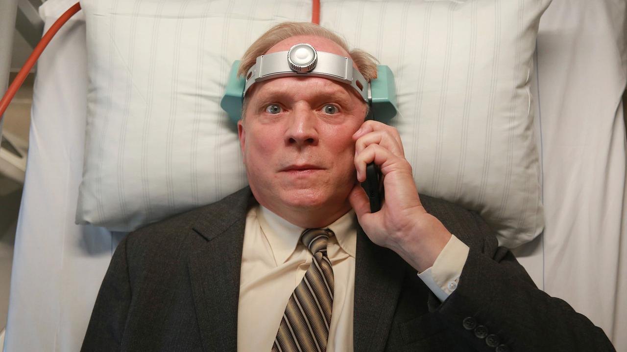 Kommissar Felix Murot im Anzug liegt im Krankenhausbett und telefoniert, während ein medizinisches Gerät um seinen Kopf angebracht ist.