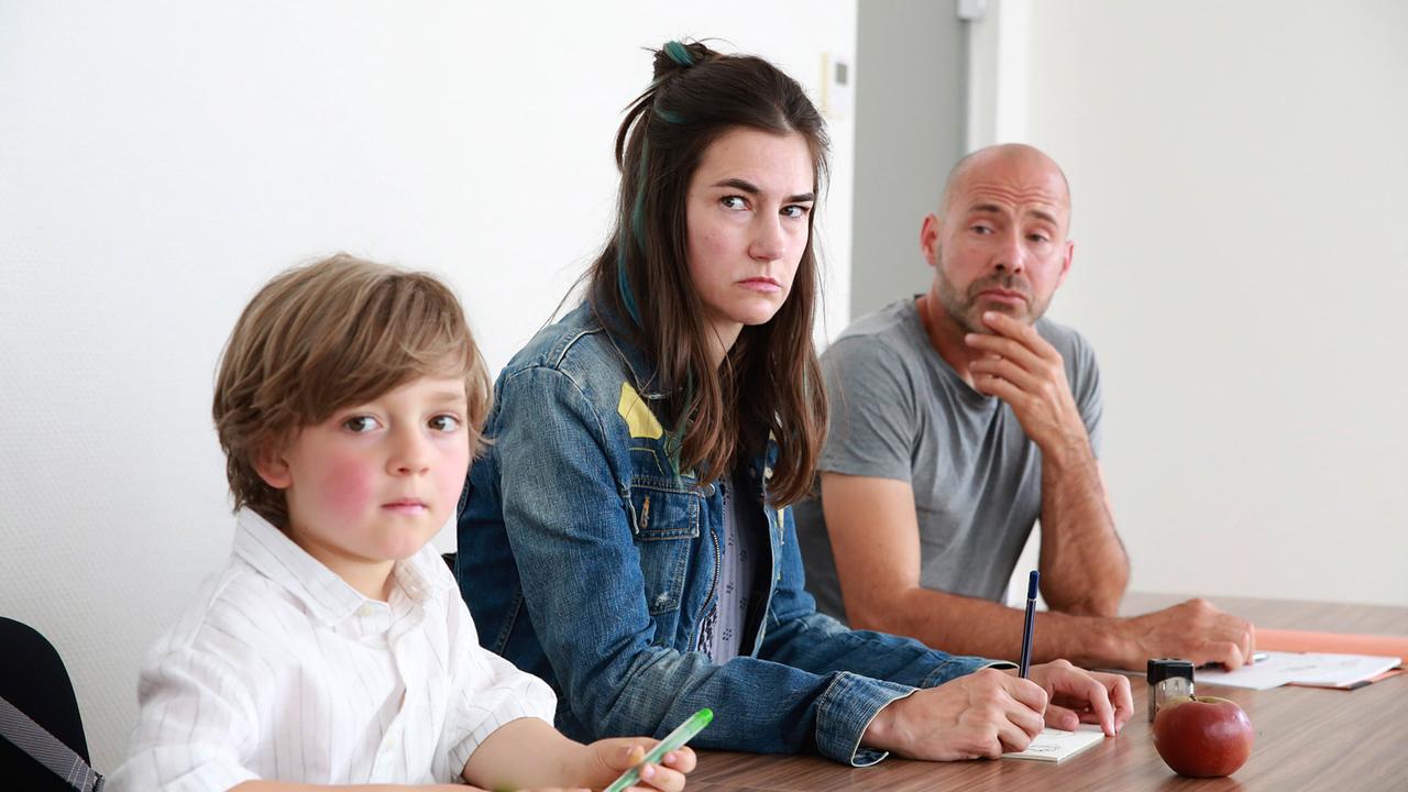 Benjamin, Eva Hütter und ein Mann sitzen gemeinsam an einem Tisch mit Block und Stift in einem modernen, hellen Raum.