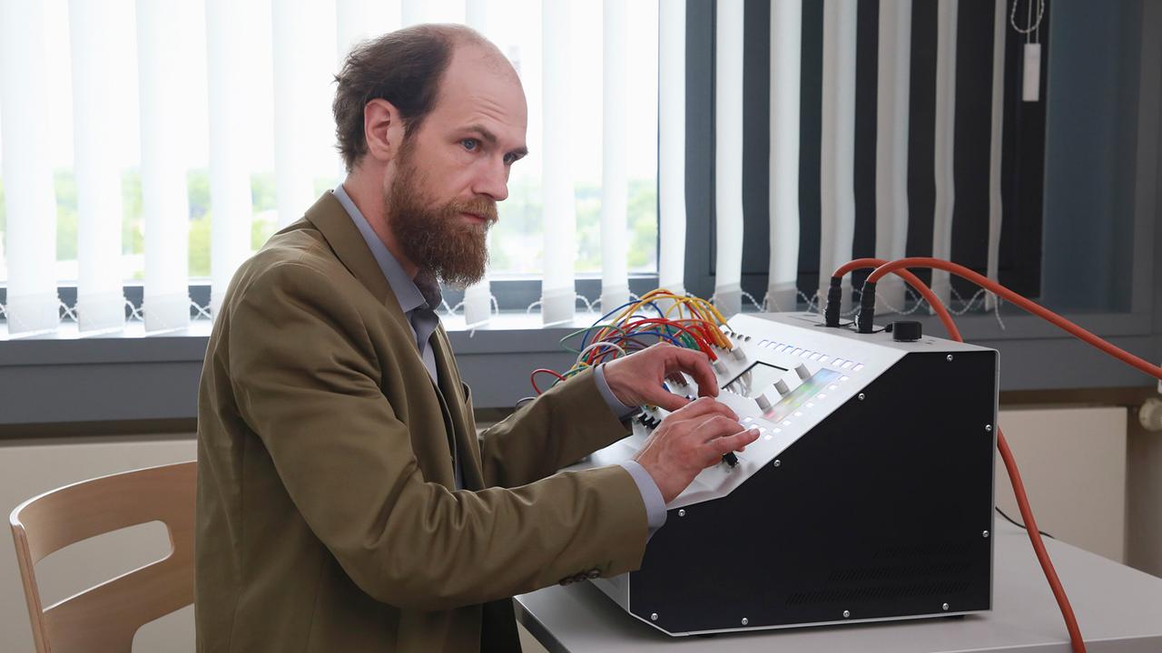 Dr Schneider bedient ein technisches Gerät mit vielen Kabeln und Schaltern in einem Krankenhauszimmer.