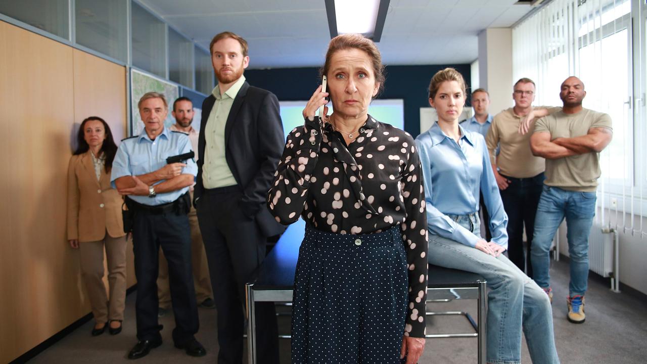 Magda Wächter steht mit ihremSmartphone am Ohr in einem Büro, während mehrere Kolleginnen und Kollegen um sie herum stehen.