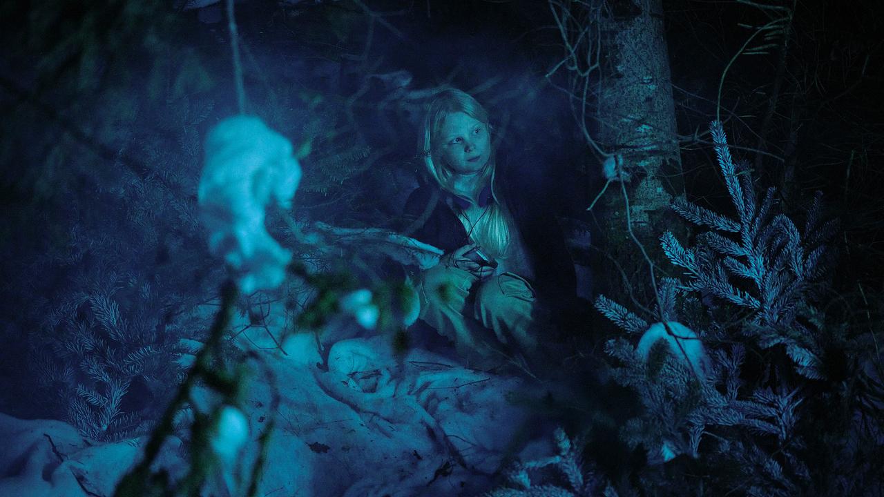 Eliza duckt sich im verschneiten, dunklen Wald zwischen dichtem Geäst.