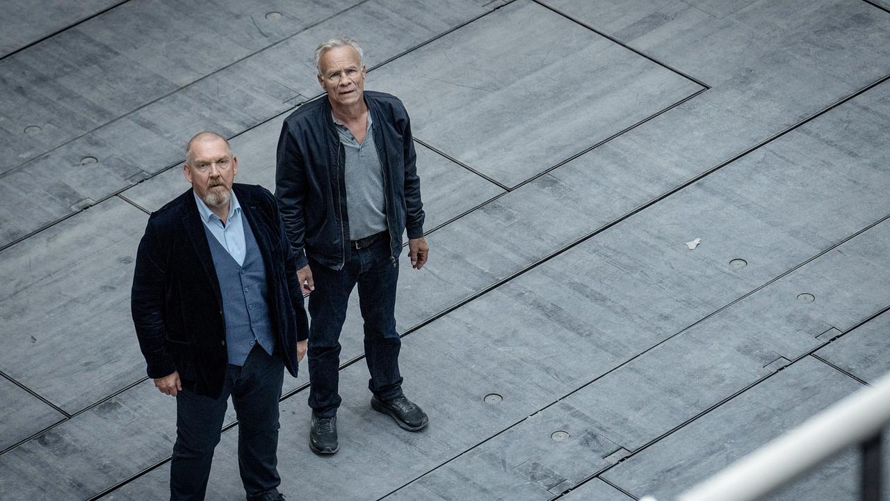 Freddy Schenk und Max Ballauf stehen auf der uf der Opernbaustelle auf einer großen grauen Plattform und blicken nach oben.