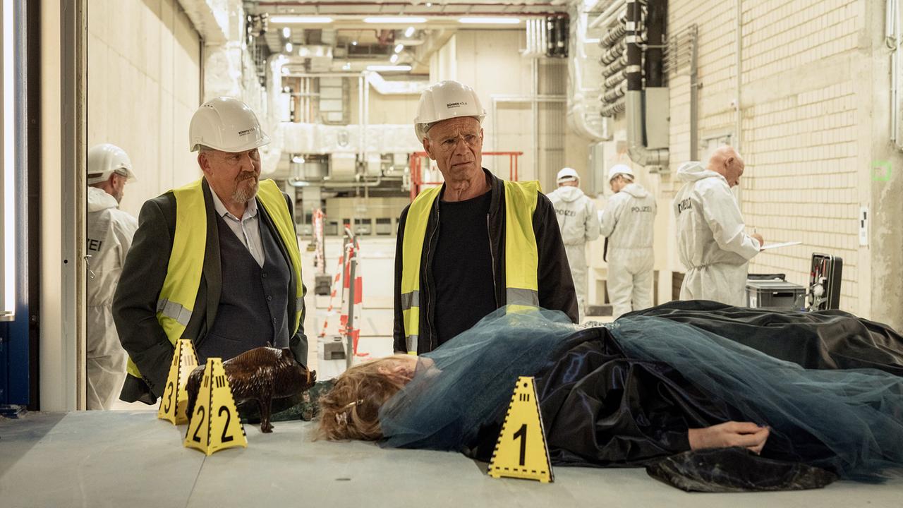 Max Ballauf (Klaus J. Behrendt) und Freddy Schenk mit Schutzhelm und Warnweste nehmen am Fundort der Leiche in einem industriellen Umfeld eine erste Bestandsaufnahme vor.