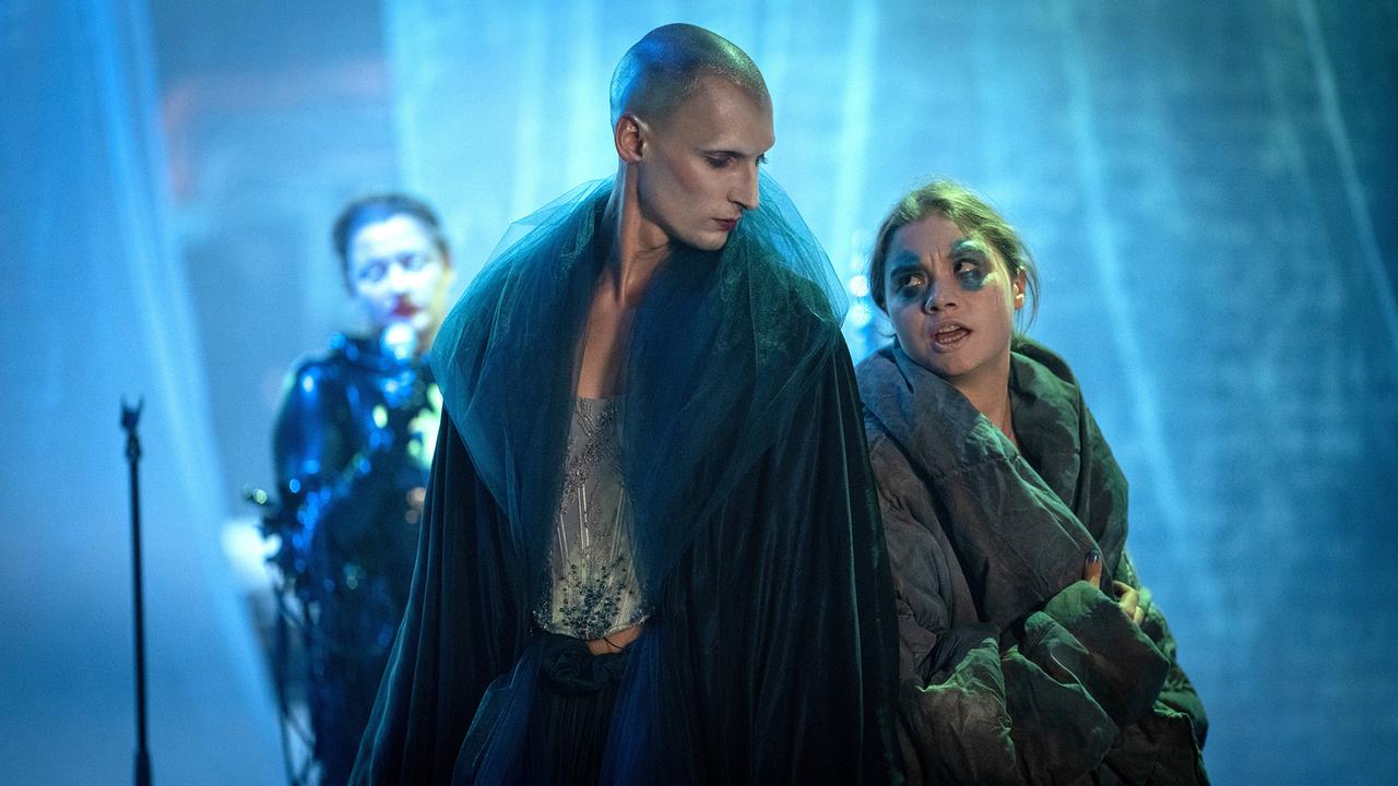 David Deycks und Valerie Schmit stehen in aufwendigen Kostümen auf einer stimmungsvoll beleuchteten Opernbühne während der Probe zu einer Metal-Oper.