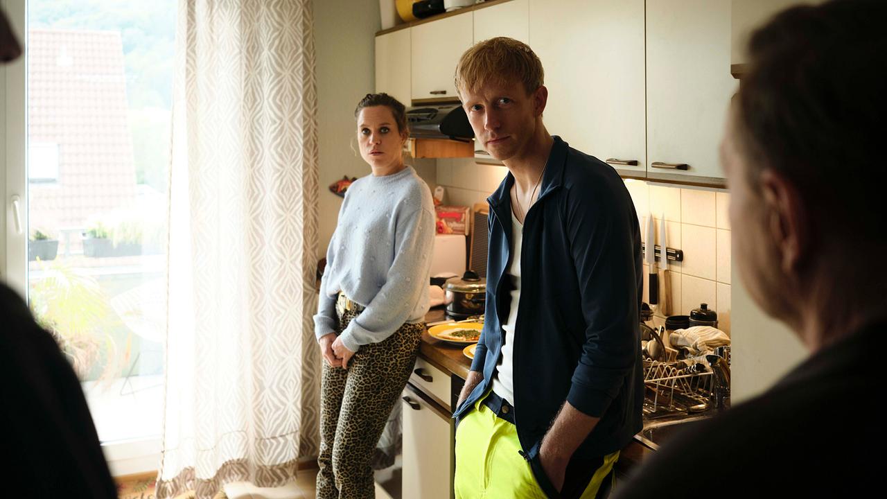 Pat und Echse lehnen an einer Küchenzeile beim Gesprächmit den beiden Kommissaren.