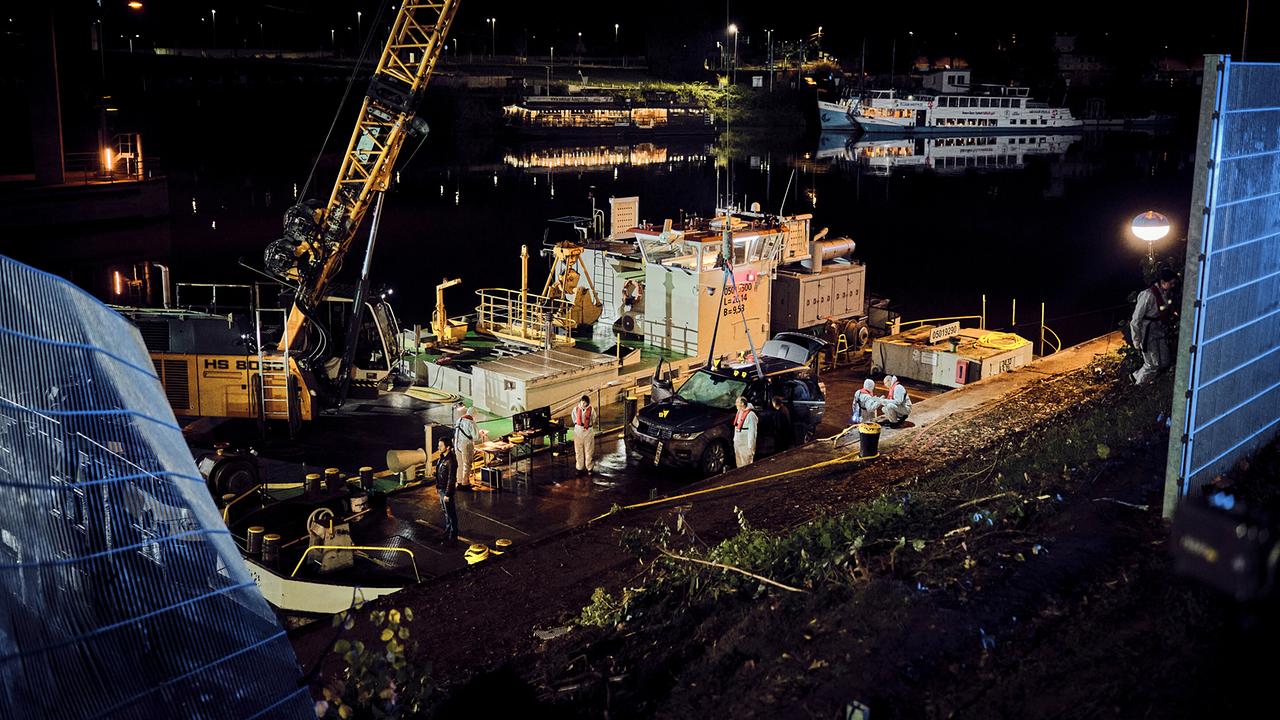 Ein Bergungsteam hebt nachts ein Fahrzeug mithilfe eines Krans aus dem Rhein.